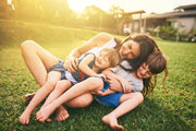 Mother playing on grass hugging her kids, bonding outside their house in the grass