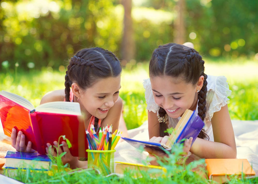 Sisters laughing, reading outside together in the summer.