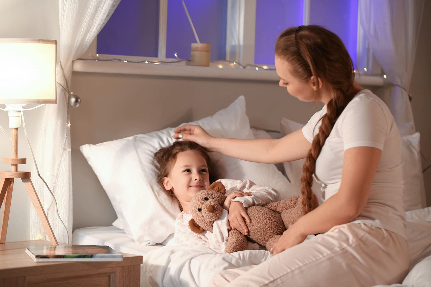 Mother sitting on her little daughters bed saying goodnight to her