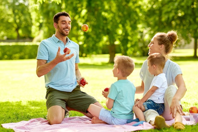 Dad jugglings apples for kids enjoyment while having a family picnik outside in summer 